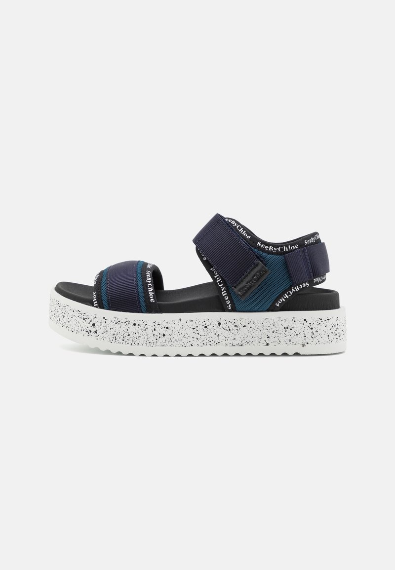 Sandale à plateforme bleu marine avec brides réglables, semelle épaisse blanche tachetée et logo SeeByChloé sur les brides et les bords.
