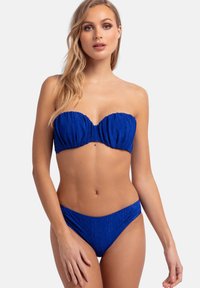 Modra bandeau bikini komplet iz lahkega, teksturiranega materiala. Zgornji del ima nabrano zasnovo, spodnji del pa ima stranske naborke za dodatno podrobnost.