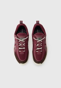 Para bordowych i brązowych sneakersów z białymi sznurowadłami, z detalami z siateczki i skóry oraz beżowymi podeszwami, widzianych z góry na białym tle.