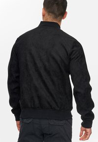 Schwarze Bomberjacke mit einer weichen, strukturierten Oberfläche. Verfügt über gerippte Bündchen und Saum, mit einem Stehkragen und ohne sichtbare Verschlüsse.