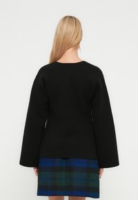 Black sweater with wide sleeves, round neckline, and a smooth texture, paired with a blue and green plaid skirt.