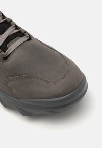Chaussure de randonnée en suede gris avec une languette en mesh rembourrée, un embout renforcé et une semelle en caoutchouc texturée pour une meilleure adhérence. Présente des lacets et des coutures gris.