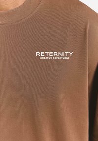 Brown short-sleeve t-shirt made from smooth fabric. Features a crew neck. Text "RETERNITY CREATIVE DEPARTMENT" in white, placed on the left chest.