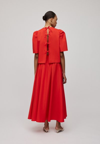 Rotes Kleid mit kurzen Puffärmeln, offenem Rücken mit drei Schleifen, tailliertem Oberteil und einem fließenden Rock. Glatte Textur und lebendige Farbe.