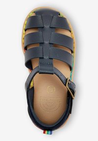 Sandal s uzavřenou špičkou, s horní částí z námořnické kůže, má design křížových popruhů a barevné pletené akcenty kolem podrážky. Zlaté embosované logo uvnitř.