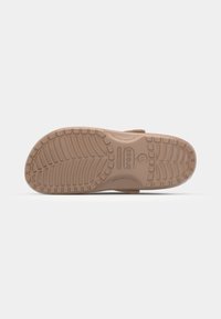 Semelle d'une sandale Crocs beige montrant une semelle texturée avec des motifs carrés et courbes, taille 11 indiquée au centre.