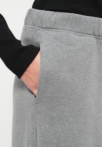 Pantalones deportivos grises hechos de tela suave, con un bolsillo lateral y una cintura elástica, mostrados junto a una camiseta de manga larga negra.