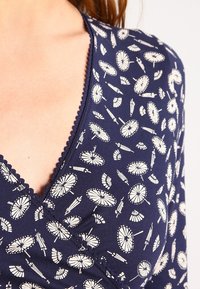 Mörkblå topp med en inslagen design, med ett vitt parasollmönster, vågig kant och mjuk tygkänsla.