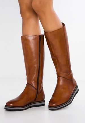 Bottes en cuir marron montantes avec une fermeture éclair sur le côté, bout effilé et semelle noire contrastante ; texture lisse avec un minimum de détails de surpiqûres.