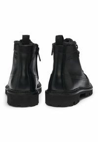 Stivaletti neri in pelle con una suola nera massiccia e texture, dotati di chiusura con zip e fodera morbida lungo il colletto.
