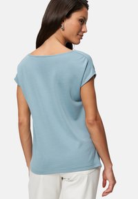 Light blue, short-sleeve top with a wide neckline and a smooth texture. Features a relaxed fit and is paired with light-colored bottoms.