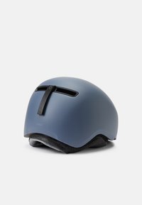 Modra matirana čelada s zaobljeno obliko, prezračevalnimi režami in črnim sistemom za pritrditev. Mehak notranji podložek. Lahka zasnova.