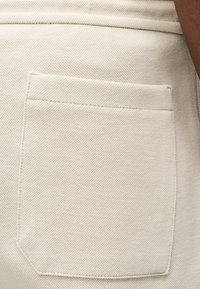 Κοντινή λήψη υφασμάτινου μπεζ παντελονιού με ορθογώνια πίσω τσέπη και εμφανείς ραφές κατά μήκος των άκρων.