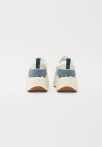 Baskets blanches avec des accents en tissu à motifs bleus, semelles en caoutchouc et un onglet de talon arrière texturé. Comprend une surface lisse et un logo de marque visible.