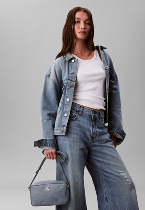 Veste en jean délavée bleu clair, coupe oversize, avec boutons pression. Associée à un jean taille haute bleu clair et un petit sac bandoulière gris.