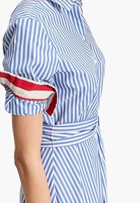 Sininen ja valkoinen raidallinen mekko lyhyillä hihoilla. Punaiset yksityiskohdat hihoissa, vyötäröstä istuva malli ja napitus. Puuvillakangasta.