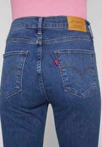 Vaqueros de mezclilla azul oscuro con una etiqueta de cuero en la parte posterior. Presentan bolsillos traseros clásicos con costura y una pequeña etiqueta roja en el bolsillo derecho.