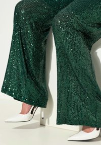 Groene pailletten flared pants met een glanzend patroon. Gecombineerd met een witte puntige hoge hak met een zwart accent detail.