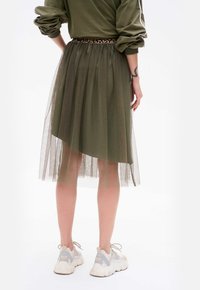 Zielona oliwkowa spódnica z tiulu o asymetrycznym dole, z leopardzim wzorem w pasie, noszona z białymi trampkami.