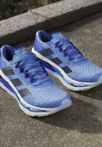 Blue athletic shoes with textured upper, prominent black stripes, and light green accents on the sole. Features a cushioned midsole and laces.