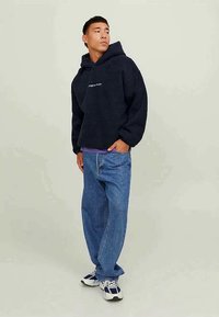 Hoodie de felpa azul-marinho com um bolso tipo canguru e logótipo, combinada com jeans de ganga azul-claro. Apresenta um corte descontraído e punhos elásticos.