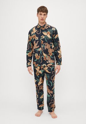 Le pyjama à manches longues présente un fond noir avec des motifs floraux et léopard dans des tons dorés, verts et marron. Texture du tissu lisse.
