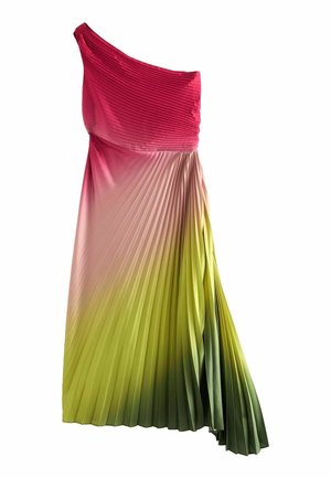 Vrouw die buiten staat bij zonsondergang, gekleed in een geplooide, asymmetrische jurk met kleurverloop van rood naar geel en groen, met open schoenen.