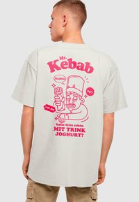 Heled värvi üle suur t-särk, millel on roosa graafiline illustratsioon kokast, kes hoiab kebabi koos tekstiga. Lühikesed varrukad, ümmargune kaelus.