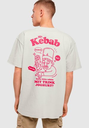 Lysfarget oversized t-skjorte med rosa grafisk illustrasjon av en kokk som holder en kebab med tekst. Kortermet, rund hals.