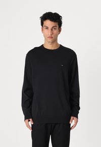Maglione nero a girocollo realizzato in morbido tessuto, con maniche lunghe e una piccola accentuazione del logo sul lato sinistro del petto. Design dritto.