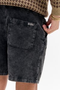 Shorts en velours côtelé noir avec une texture ribbed et une poche arrière. La poche arbore le texte "BDG" dans une couleur contrastante.