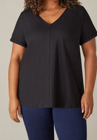 Svart kortärmad V-ringad topp med uppvikta ärmar, tillverkad av mjukt material. Har en diskret mittsöm och en avslappnad passform.