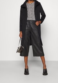 Černý kabát s vysokým límcem, v kombinaci s bílým a černým vzorovaným topem. Černé kožené kalhoty do culottes a otevřené černé lodičky na vysokém podpatku. Malá kabelka.