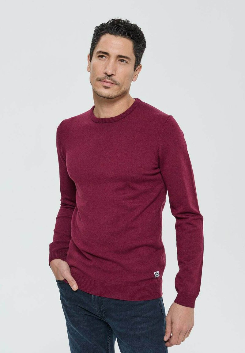 Pull-over en maille bordeaux à col ras du cou, avec des poignets et un ourlet côtes, doté d'un petit logo brodé en bas à gauche.