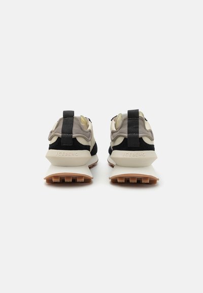 Zapatillas que combinan materiales en negro, gris y crema, con acentos texturizados y una suela blanca gruesa. Branding minimalista visible.