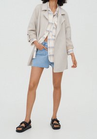 Lys grå blazer, ternet skjorte med blå accenter, denim shorts og sorte sandaler. Fokuser på tekstur og lagdeling.