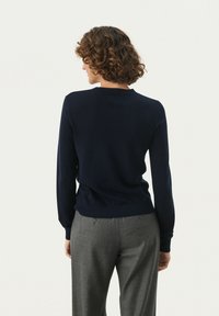 Dunkelblaues Sweatshirt mit rundem Halsausschnitt und langen Ärmeln, aus weichem Material. Kombiniert mit hellgrauen, taillierten Hosen, die ein einfaches Design zeigen.