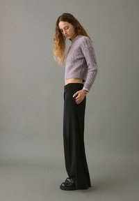 Maglione corto di un leggero viola con trama a costine, abbinato a pantaloni a gamba larga neri e scarpe nere, che mostra una vestibilità rilassata.