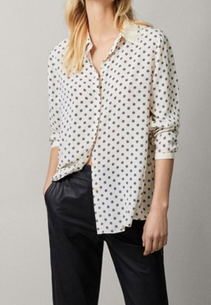 Biała koszula w czarne kropki, z zapinaniem na guziki z przodu, kołnierzykiem i długimi rękawami, zestawiona z czarnymi spodniami, prezentująca gładką fakturę tkaniny.