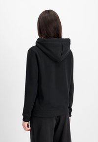 Sudadera negra con capucha ajustable, puños y dobladillo acanalados. Tejido suave y texturizado, con un diseño sencillo sin logotipos visibles.