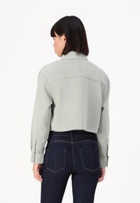 Kort, lys grønn denimjakke med krage og knappede mansjetter, brukt over mørkeblå, tettsittende jeans.