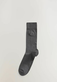 Siva pamučna čarapa s rebrastim rubom, glatke teksture i zaobljenim prstima. Ima mali, utisnuti logotip blizu gležnja.