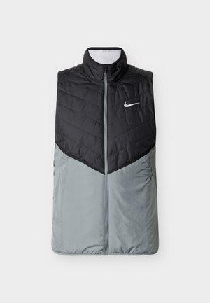 Juoda ir pilka be rankovių Nike pūkinė liemenė su aukštu apykakliu ir priekinio užtrauktuko uždarymu, ant krūtinės su Nike „swoosh“ logotipu.