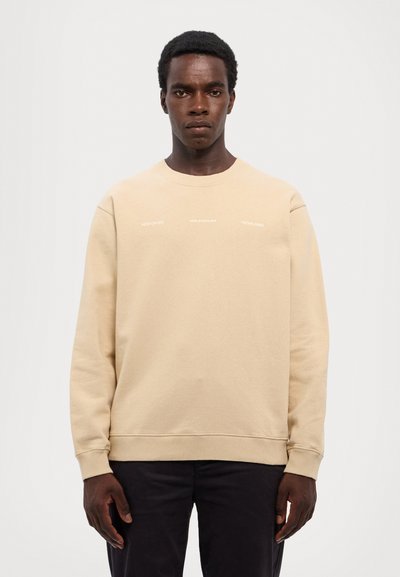 Béžová mikina s kulatým výstřihem, dlouhými rukávy a žebrovanými manžetami. Na hrudi se nachází bílej potisk s textem v čistém, moderním písmu.