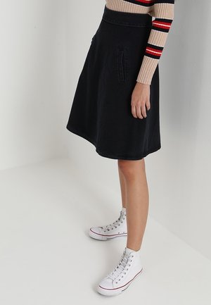 Zwarte denim A-lijn rok met zijzakken, gedragen met een gestreepte trui en witte hoge sneakers. Heeft een gladde textuur en een knielengte snit.