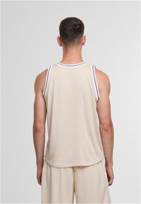 Beige ermeløs atletisk tanktopp med kontrasterende marineblå stripe langs utringningen og armene, laget av mykt, lett stoff.