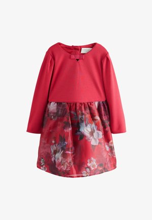 Röd långärmad klänning med överdel i solidt tyg, med en båge som detalj, och en nederdel med blommönstrad, genomskinlig lager.