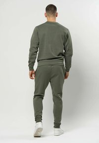 Olivengrønn genser og matchende joggebukser laget av mykt materiale, med ribbestrikkede mansjetter og kant, kombinert med hvite joggesko.