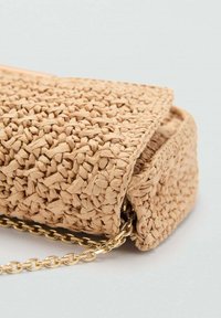 Tkana bež ručna torba s teksturiranom površinom, pravokutnog oblika i zlatnim lančićem za nošenje. Zatvaranje na vrhu.