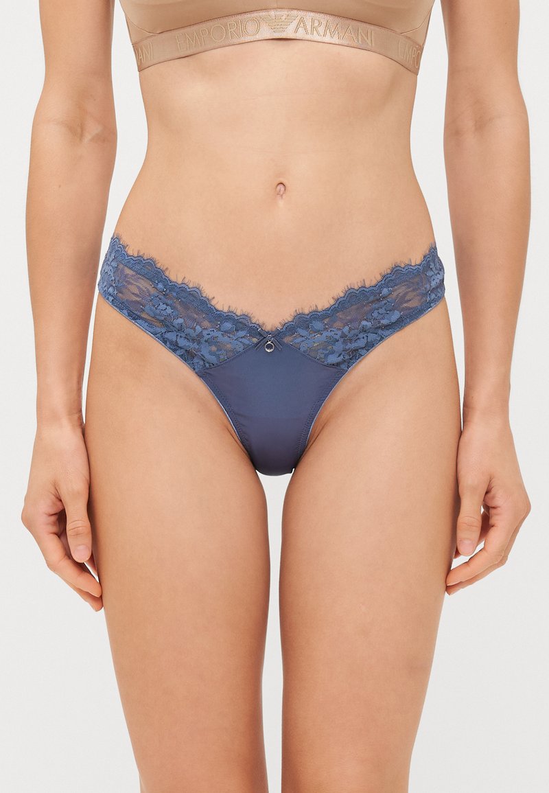 Marineblauwe string met kantafwerking, voorzien van een bloemenpatroon en een kleine decoratieve accent aan de voorkant. Zacht, glad materiaal.